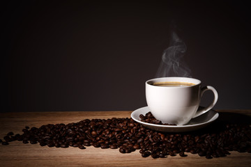 Steaming coffee in cup put on coffee beans on wood background with copy space.