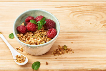 Homemade granola in a bowl with raspberries on a wooden table.