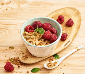 Homemade granola in a bowl with raspberries on a wooden table.
