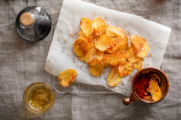Homemade potato chips strewn with rock salt and paprika served on linen cloth with sous and beer.