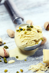 Pistachio ice cream scoop with chopped nuts and white chocolate on a rustic background.