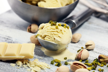 Pistachio ice cream scoop with chopped nuts and white chocolate on a rustic background.