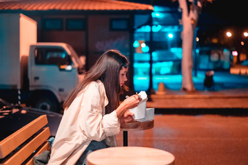 The girl is eating fast food, on the street of the night city