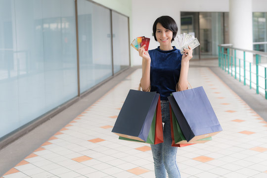 Young Beautiful Asian Woman Shopping With Credit Card And Money, And Holding Color Full Shopping Bags In Her Arms With Smiling Face..