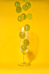 Grapes falling into a champagne glass with yellow background