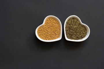 seeds of mustard and herbs in heart-shaped bowls on a black background