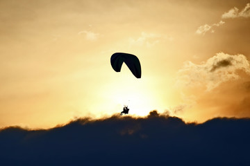 Paraglider flying on a wing in the sky against the setting sun
