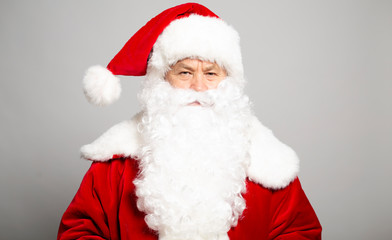 Portrait of serious man in Santa Clause costume looking at camera on grey background, Christmas and New year concept