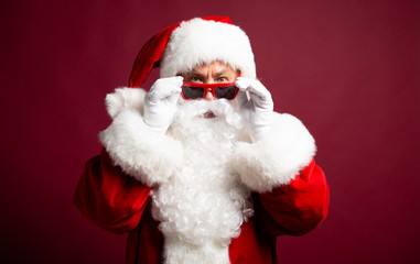 Surprised Santa Clause wearing sunglasses and looking at camera on red background