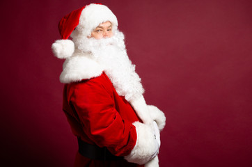 Portrait of man in Santa Clause costume with crossed arms posing on red background, Christmas and New year concept