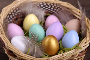 Wicker basket with colored Easter eggs, feathers, decorative chicken and a wish on a wooden label on a dark wooden background.