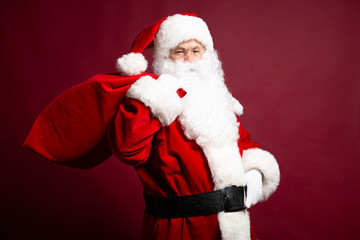 Portrait of grandfather in Santa Clause costume with gift sack on back posing on red background, Christmas and New year concept