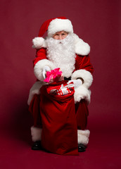 Man in Santa Clause costume sitting with gift sack on red background, Christmas and New year concept
