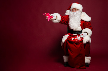 Happy Santa Clause giving present while holding with gift sack on red background, Christmas and New year concept