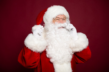Portrait of man in Santa Clause costume talking on smartphone and smiling on red background, Christmas and New year concept