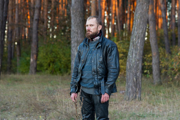 Naklejka na ściany i meble Motorcyclist in a leather jacket and pants standing in a forest