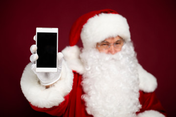 anta Clause holding and shows smartphone on red background, Christmas and New year concept