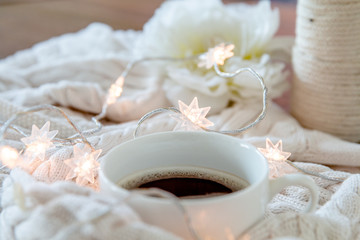 Fototapeta na wymiar Cup of coffee wrapped in whie cozy sweater with twinkle lights