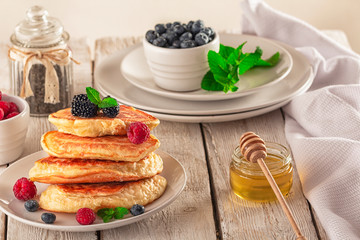 Delicious ready-made golden pancakes with fresh blueberries, raspberries and honey