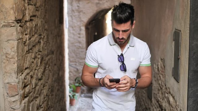 Young male tourist exploring old italian town of Cervo in Liguria region, using cell phone