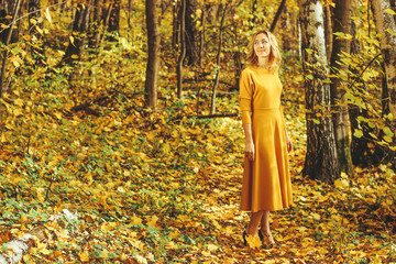 Young beautiful girl in a yellow long dress walks in autumn park with fallen leaves