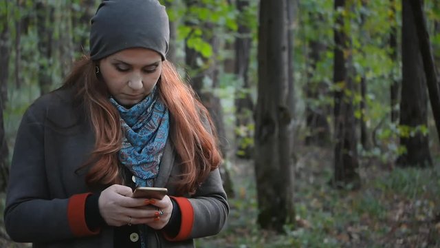 girl with stands in the forest in the autumn forest and writes sms