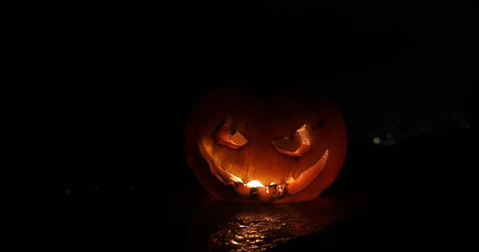 Horror Halloween concept. Close up view of scary dead Halloween pumpkin glowing at dark background. Rotten pumpkin head. Selective focus