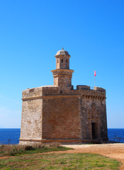 Fototapeta na wymiar The Sant Nicolau Castle in ciutadella menorca on the cliffs with blue summer sea and blue sky