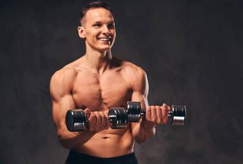 Fototapeta na wymiar Young shirtless bodybuilder with muscular body doing exercise with dumbbells on dark background.