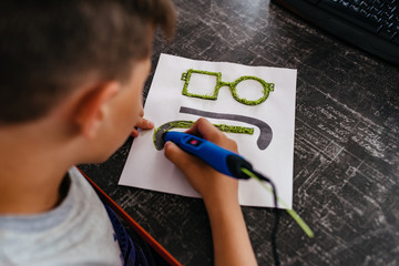 Teenager boy draws different things by 3d pen with a blue plastic handle. Mathematics. Engineering....