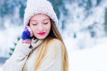 Close-up of a girl's face in a sweater and a hat that closed her eyes against the background of snow and wood