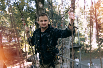 man, climbing gear in an adventure park are engaged in rock climbing or pass obstacles on the rope road, arboretum, insurance, attraction, amusement park, active recreation, autmn