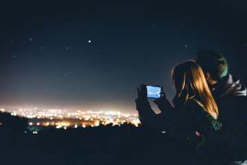 Loving couple is stand on the terrace by the wooden railing. look to distance, the lights of the...