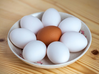 One brown and white eggs in a ceramic dish on a wooden table