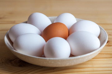 One brown and white eggs in a ceramic dish on a wooden table