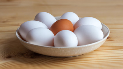One brown and white eggs in a ceramic dish on a wooden table