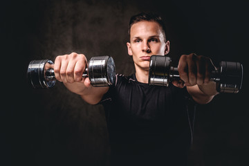 Fototapeta na wymiar A young bodybuilder wearing sportswear doing exercise with dumbbells on dark background.