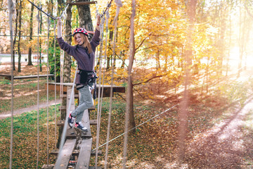 happy girl, women, climbing gear in an adventure park are engaged in rock climbing or pass obstacles on the rope road, arboretum, insurance, attraction, amusement park, active recreation, autmn