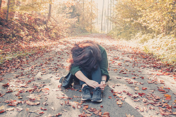 Brunette girl sitting on the ground with her head bowed to her knees in the autumn forest, autumn mood concept