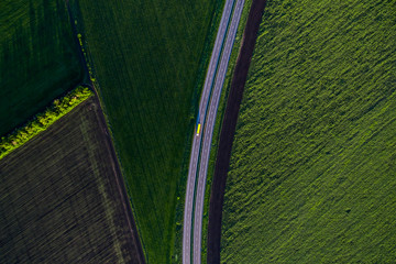 yellow truck driving on asphalt road along the green fields in rural landscape. Road seen from the...