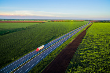 Dump trucks carrying goods on the highway. Red truck driving on asphalt road along the green fields. seen from the air. Aerial view landscape. drone photography.  cargo delivery