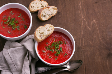Delicious vegan soup of baked tomatoes and sweet peppers with herbs in a white plate on a wooden background, top view, free space, horizontal