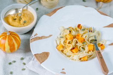 Pasta with pumpkin in a cream sauce in a craft bowl. Handmade ceramic plate. Autumn meal for lunch.