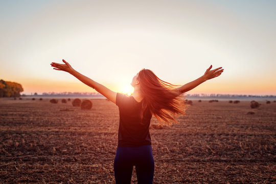 Happy young woman raising opened arms in autumn field admiring the view. Woman feeling free.