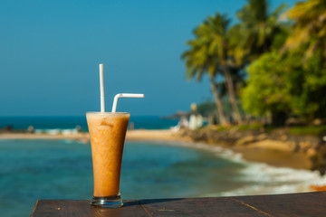 Glass with fruit juice fresh on the background of the sea and palm trees