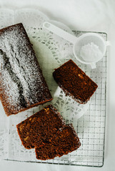 Chocolate cake with nuts inside cut into slices on cooling rack. A mini sieve with powdered sugar. Directly above, white background.