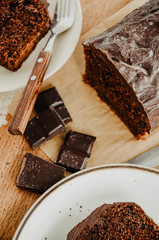 Chocolate pound cake slices on white plates. Brown toned, wooden background. Chocolate bar broken into pieces.