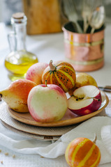 Still life with small pumpkins, apples and pears on a ceramic plate. Autumn still life in bright colors. Vegetables and fruits on the table with a white tablecloth.