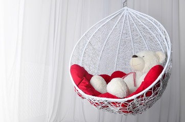 toy bear and decorative swing with red pillows. cozy place to relax