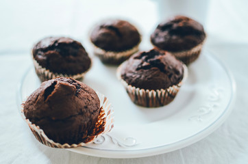 Mini chocolate muffins on white plate. White background, low angle shot.
